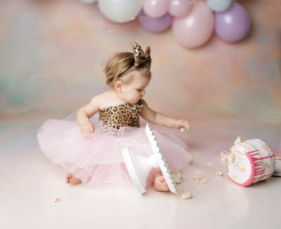 Little girl looking at cake that fell onto floor with purple balloons behind her