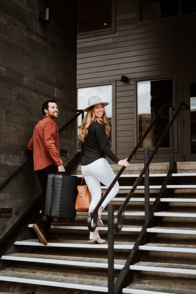Stylish couple with suitcase climbing hotel stairs, captured by Breckenridge branding photo and video content team.