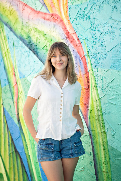 high school senior girl with jean shorts and white top in front of painted mural in winter garden shot by orlando senior photographer Melissa Vinsik