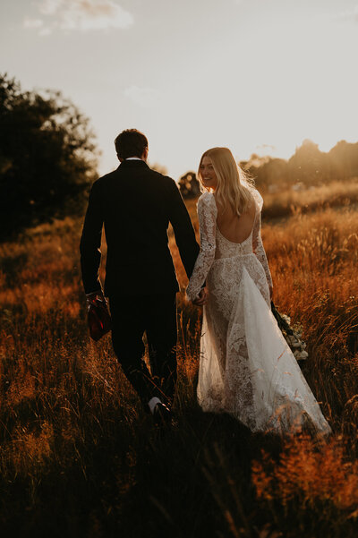 A wedding couple walk towards the sunset whilst the bride looks back at the camera. 