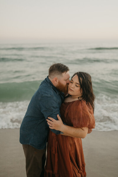 man kisses woman on cheek on beach