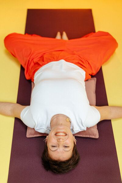 Leslie est installée sur son tapis de yoga dans la posture du papillon allongé. La photo est prise de haut.  