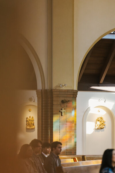 People sitting in church pews with colorful light coming in from the windows behind them