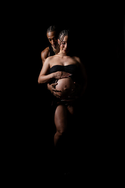 Image of a man holding a pregnant woman in a studio setting with black backdrop.
