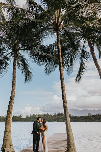 Bride and groom kissing on dock under palm trees