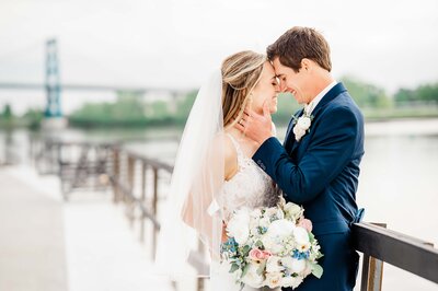 groom holding brides chin while standing forehead to forehead and smiling
