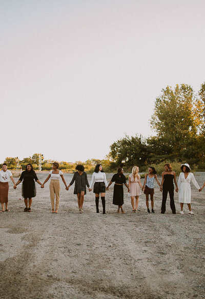 A diverse group of women holding hands outdoors, symbolizing support and unity.