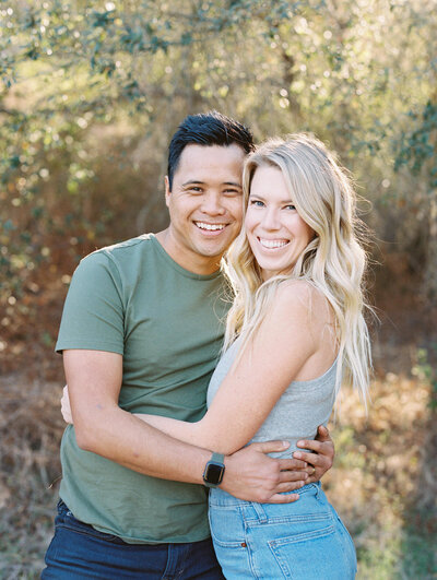 a sweet photo of a young couple looking at the camera while embracing and smiling