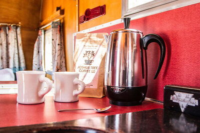 Location Branding photo closeup of vintage coffee pot with two white coffee mugs on red counter Gatos Trail Ranch