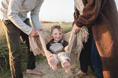 Child being swung in a blanket by his parents during a sunset beach photoshoot in bournemouth