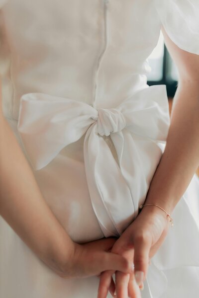 Close-up of an elegant satin wedding dress featuring a handcrafted bow detail at the waist