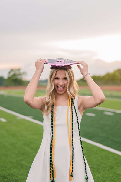 Excited high school senior making a fun face while grabbing her cap, photographed by Pittsburgh Senior Photographer Bree Stewart of LLP.