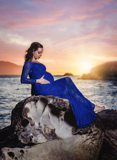 Pregnant woman in red dress embraces her belly for maternity portrait