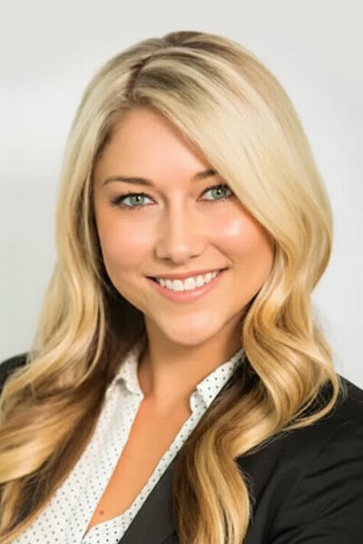 Headshot of a young blonde woman wearing a black blazer over a white blouse.