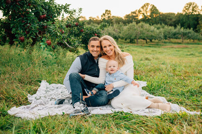 Expecting parents with foreheads together, sitting on rock at beach at sunset in Niantic, CT