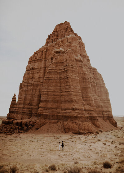 Bride and groom stand beneath a giant sandstone monolith in the desert