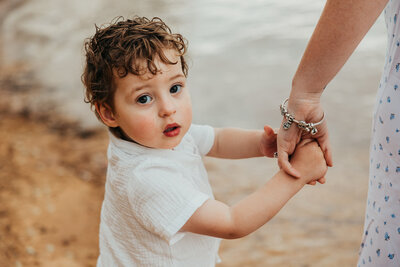 Young-toddler-holding-his-mums-hand-looking-directly-at-the-camera