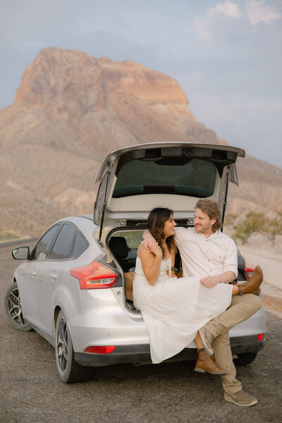 couple laughing and smiling at each other during their adventure session on a mountain top