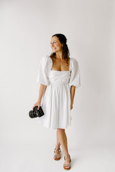Indianapolis Lifestyle Newborn Photographer Caitlyn Brady holding camera and smiling while looking over shoulder