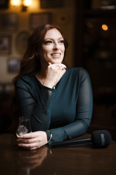 Image of Sarah Kenyon on looking out of window holding a dram with microphone on the table