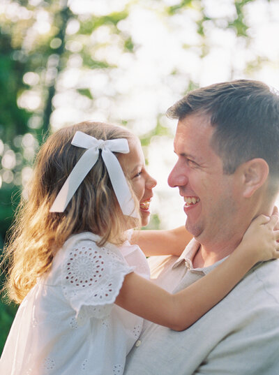 Father holds 6 year old daughter as they giggle together in the soft morning light.