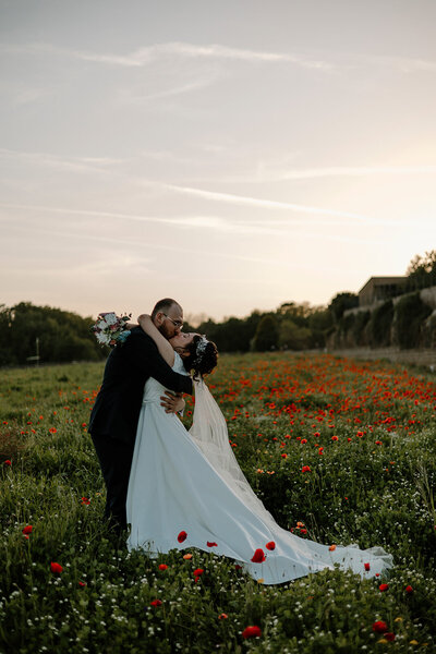 a bride and groom kissing in a red wildflower field