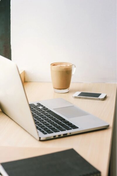 Laptop, phone, and coffee on a wooden desk, symbolizing focus and flow during virtual coaching sessions
