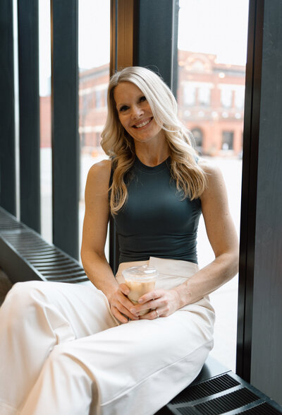 Stacie relaxing in front of a window with an iced coffee on her lap