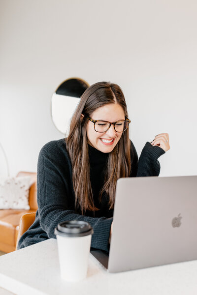 Morgan, a wedding and elopement photographer and photography educator, smiling while working on her laptop, featured on the Education for Photographers page, offering coaching, workshops, and resources.