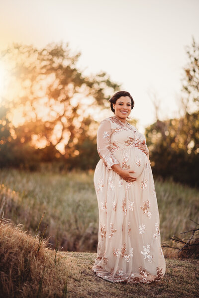 Pregnant woman holding belly in a red dress at sunset posing for a maternity session in Brentwood, CA 94513