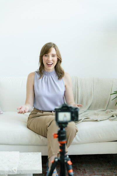 Kelsey sitting on a couch recording an video of herself with a camera on a tripod
