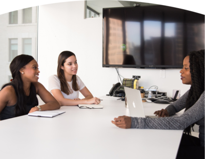 Two female students engaged in a conversation with a leadership coach in her office, highlighting the personalized coaching and mentorship offered at the Center for Leadership Excellence.