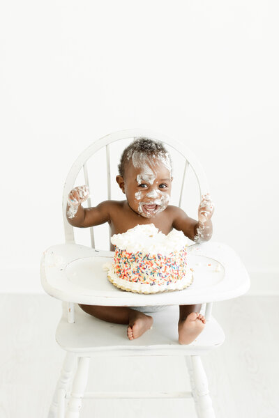 One year old baby boy celebrates his first birthday with frosting smeared across his face during cake smash portrait session