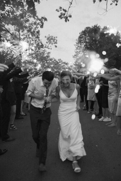 Newlyweds run through tunnel of wedding guests holding sparklers