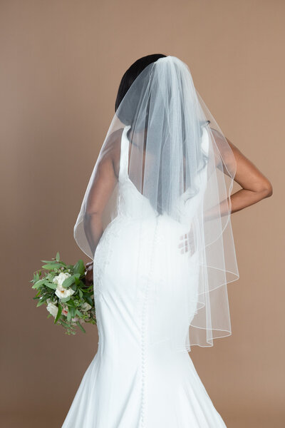 Bride wearing a fingertip length veil with serged edge and holding a white and blush bouquet