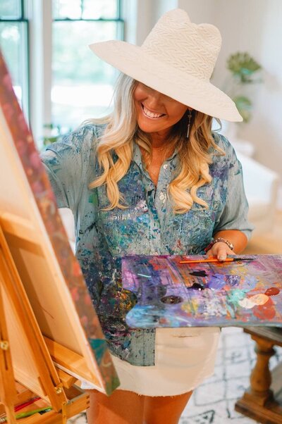 Katie, spiritual entrepreneur coach, smiling while painting, radiating vibrant energy and creativity.