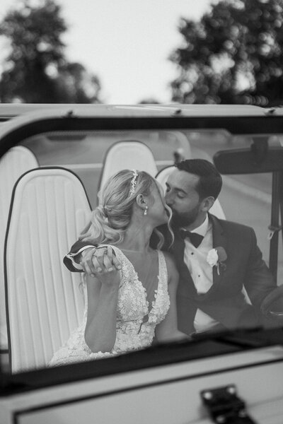 Black and white photo of the bride and groom kissing in a car