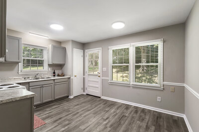 Bright kitchen featuring gray cabinets, granite countertops, wood-look flooring, and a back door with large windows.