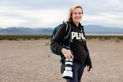Photographer holding her camera with mountains in the distance.