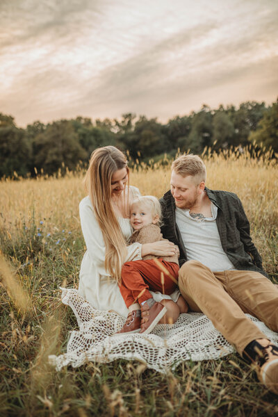 A family in a field sitting together on a crocheted blanket in Blacksburg, Virginia.
