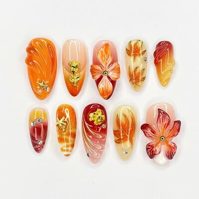 Set of fall press-on nails in orange and red with floral designs, gold accents, and gemstone details, styled for a bold autumn manicure.