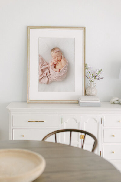 A newborn photo by Christy Johnson matted and framed to display on a credenza