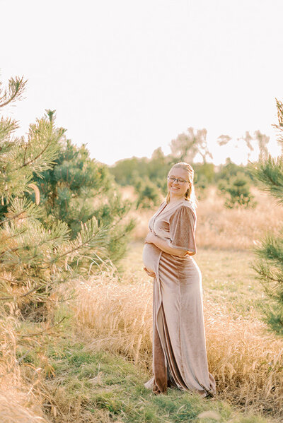 Pregnant person in pink dress at a Christmas tree farm