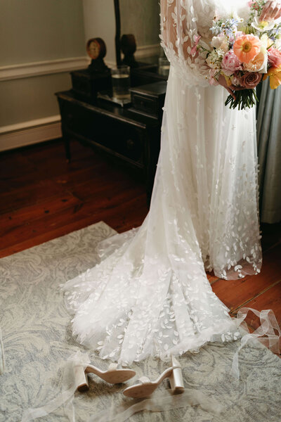 Close up view of delicate wedding dress skirt, wedding bouquet, and heels