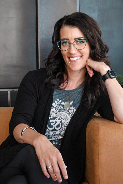 A girl with glasses sitting on a couch with her arm propped on the side of the couch