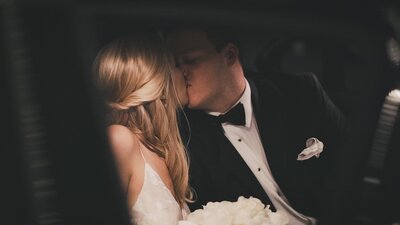 A bride and groom kissing in the back of a limo during their wedding celebration.