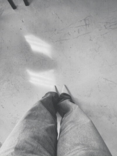 A person's legs, wearing wide leg jeans and pointed toe heels, standing on textured cement floor with soft light creating reflections on the surface.