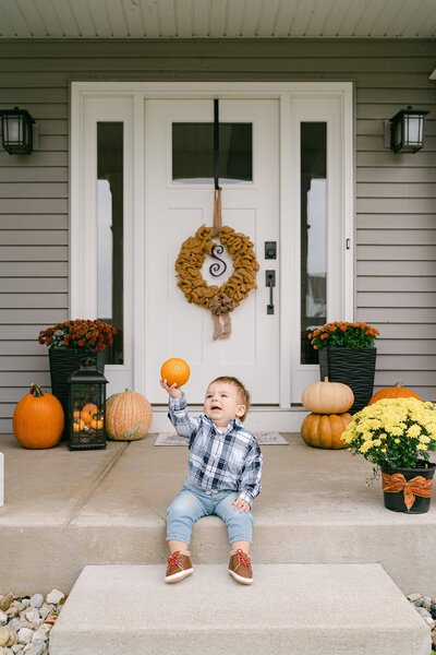 little boy sitting on his front porch holding a pumpkin