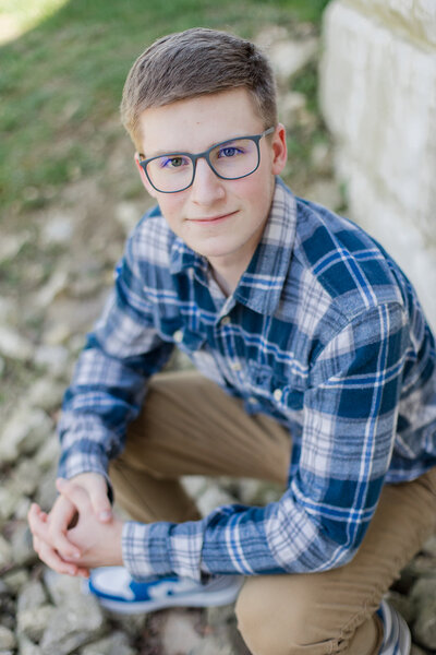 Senior guy squatting with his hands clasped while smirking at the camera. Photo by Marysville, OH senior photographer Amanda Lauren Collective