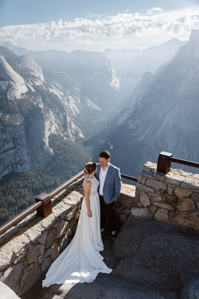 A newlywed couple with their arms around each other smiling at an overlook in Yosemite